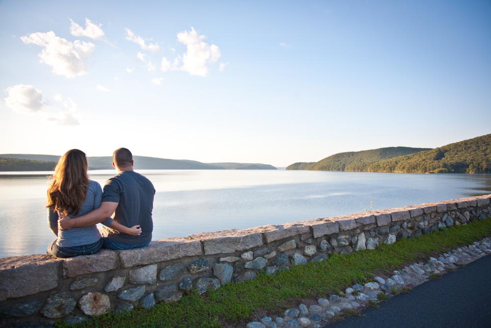 Couple sitting on low stone wall overlooking peaceful lake with rolling hills in the background