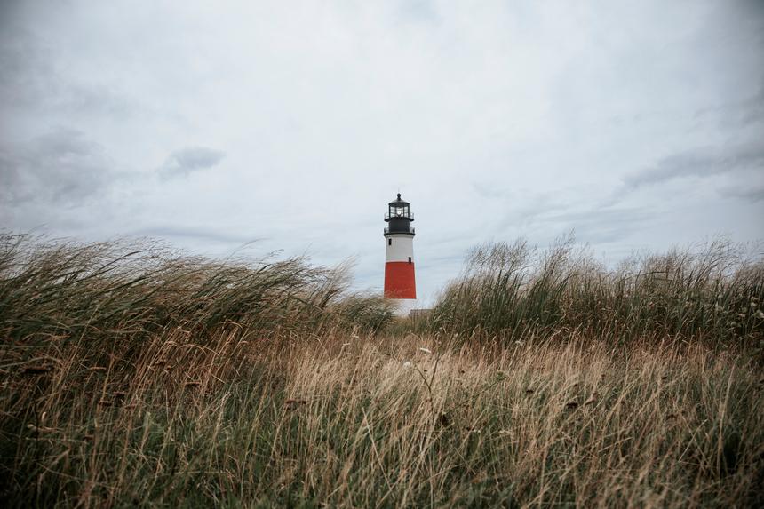 A red and white lighthouse as seen in between tall grasses on an overcast day.