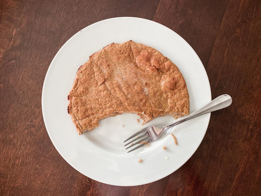 A large banana pancake on a white plate resting on a wooden table.