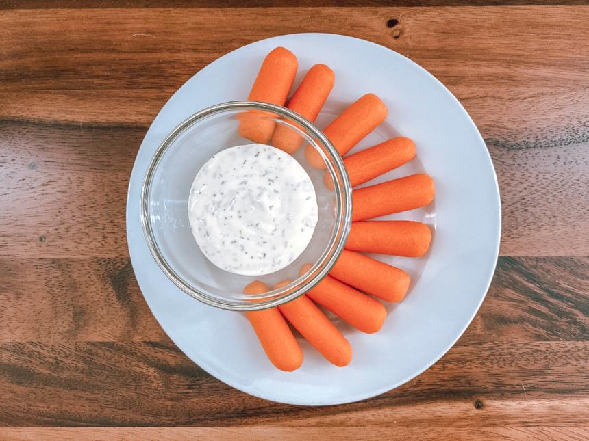 A white plate with baby carrots and a dipping container filled with Dill Dressing.