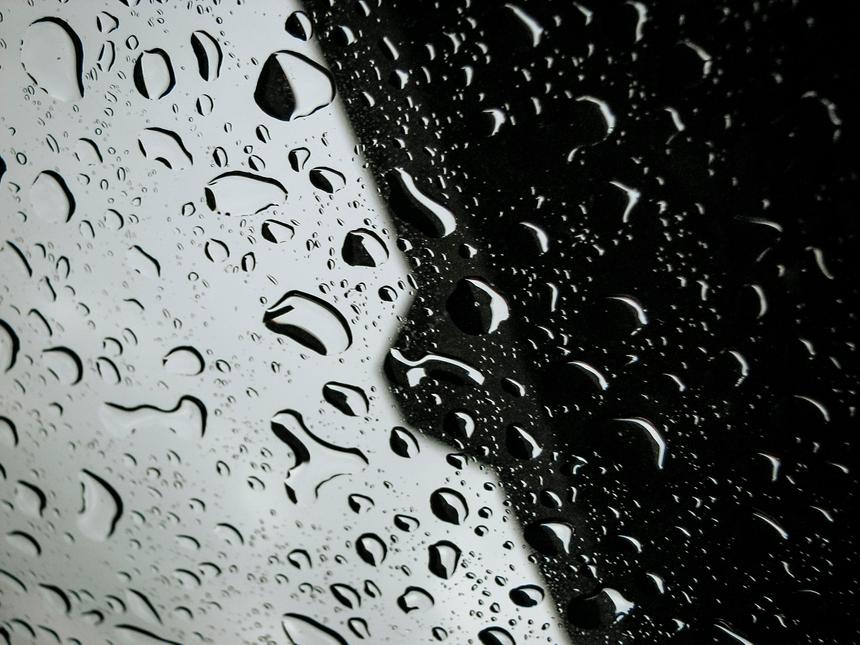 An abstract view of water droplets on a pane of glass with half in shadow and half in light.