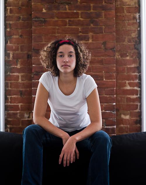 Woman with curly hair sitting in front of red brick wall