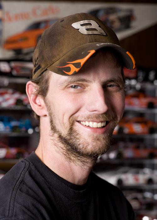 Man smiling standing in front of nascar car collection