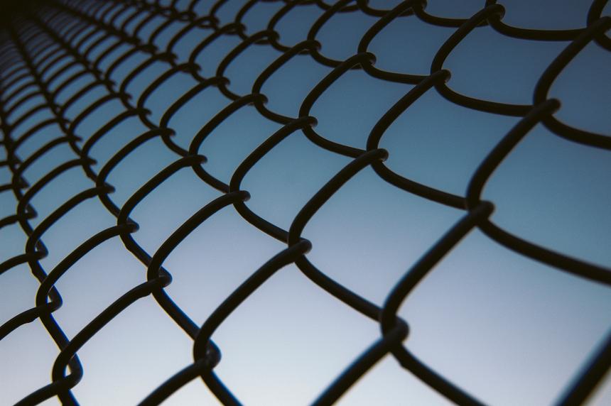 An up-close and abstract view of a chain link fence with a darkening blue sky behind it.