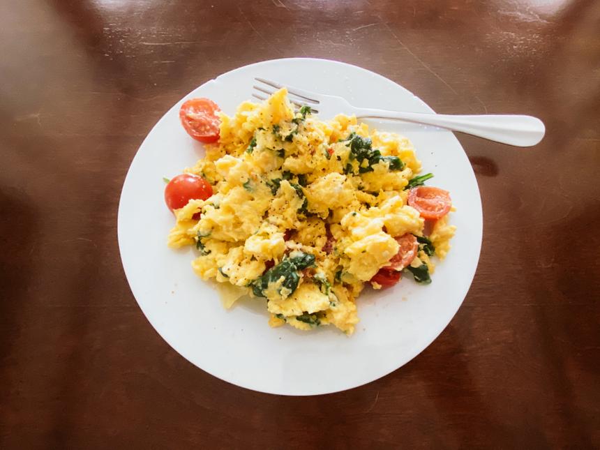 A white plate with scrambled eggs, spinach and tomato.