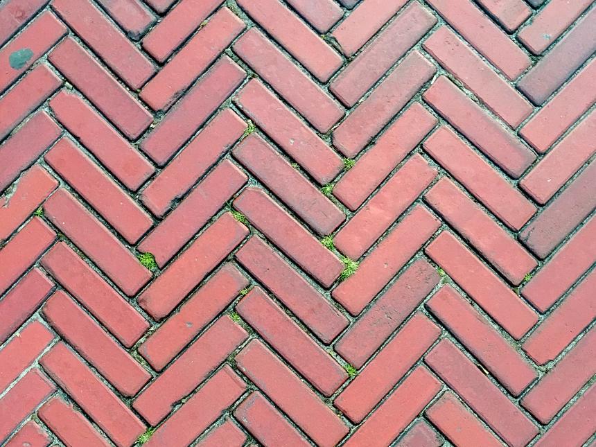 Up close view of thin red bricks laid out in a herringbone zigzag pattern.