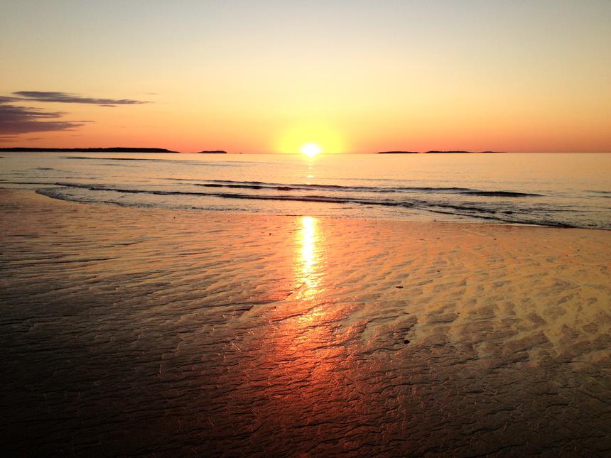 Sunrise over a beach with trails in the sand from the retreating tide.